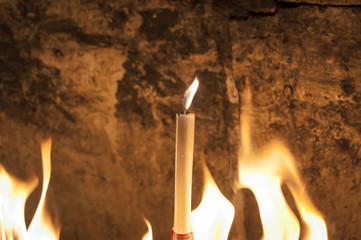 Blaze of fire with a lonely candle and a stone wall on the background inside the Church of the Holy...