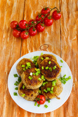 Roasted chicken cutlets with green onion on white plate and small cherry tomatoes on wooden background. Top view.
