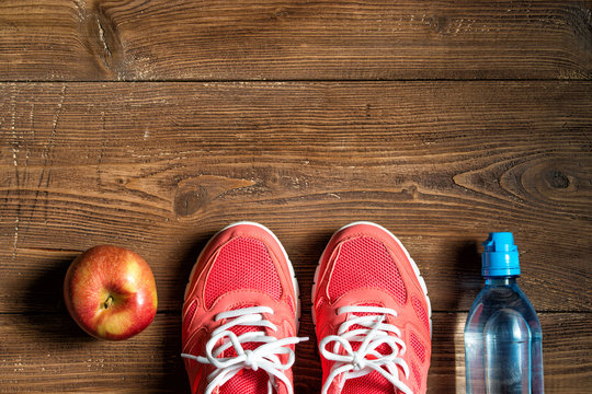 Fitness concept, pink sneakers, red apple and bottle of water on wooden background, top view