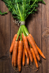 Bunch of fresh carrots with green leaves on wooden table, top view