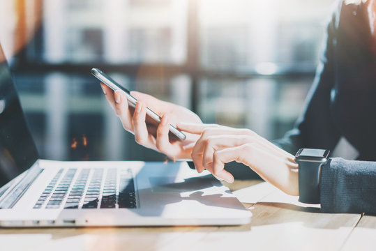 Photo Woman Working Modern Smartphone and Wearing Generic Design Smart Watch.Female Hands Touching screen phone.Manager Work Process.Laptop on the wood Table.Horizontal,Burred background. Film effects