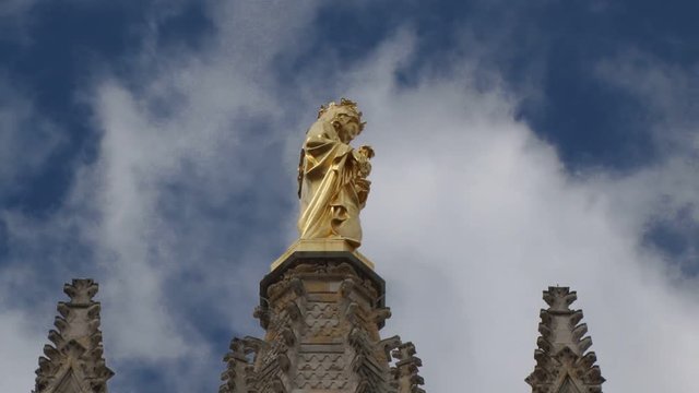 Statue of the Virgin Mary on top of the Pey Berland Tower in Bordeaux Cathedral. Clouds flot past in the background