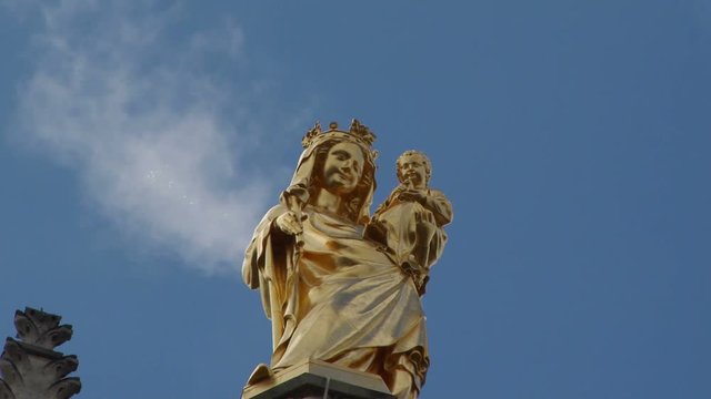 Statue of the Virgin Mary on top of the Pey Berland Tower in Bordeaux Cathedral. Clouds flot past in the background