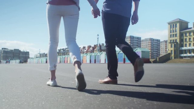  Happy romantic couple holding hands as they walk past colourful beach huts