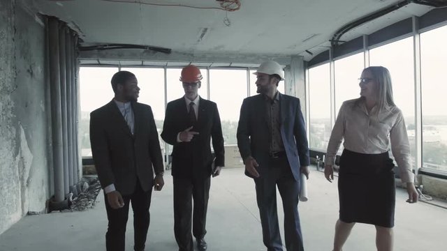 Team of architects discussing the implementation of their new project of furnishing an office building in a perspective district of the city. Three men in business suits and beautiful woman with the