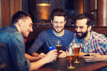male friends with smartphones drinking beer at bar
