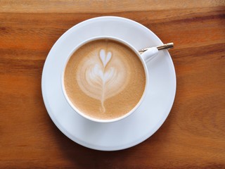 Top view of latte art coffee with heart pattern in a white cup on wooden background.