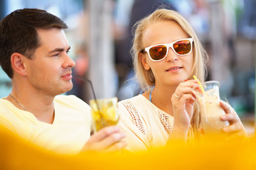 Young couple relaxing with refreshing drinks in long glasses on summer vacation with focus to an attractive woman wearing sunglasses