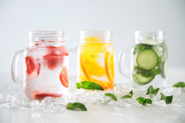 Fototapeta na wymiar Close focus on first jar Healthy fresh cool homemade lemonades with sparkling water strawberry, cucumber,mint and orange isolated in smashed ice cubes on wooden table