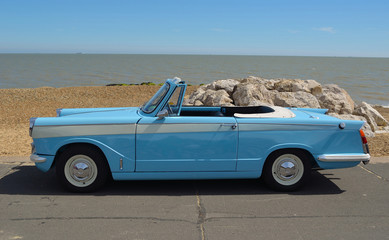 Classic light Blue Triumph Herald open top motor car parked on seafront promenade.
