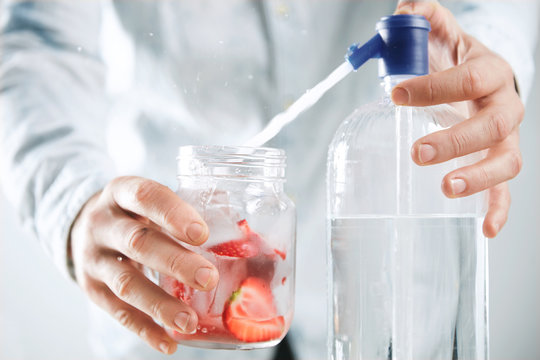 Close focus bartender makes homemade lemonade, pours sparklig water from syphone to rustic jar with strawberry slices and ice cubes inside Cool down healthy summer beverage