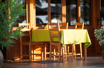 Colorful outdoor table at an open-air restaurant laid with a yellow tablecloth and wooden chairs