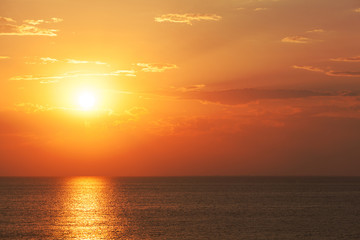 Spectacular orange tropical sunset over a calm ocean with a beam of light reflected on the calm water