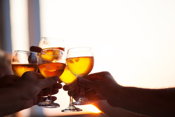 Group of people toasting each other with glasses of white wine at a celebration party, close up of their hands against a bright window with copy space