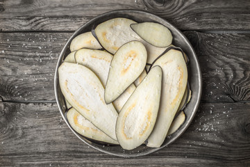 Sliced eggplants with salt in the metal plate on the wooden table top view