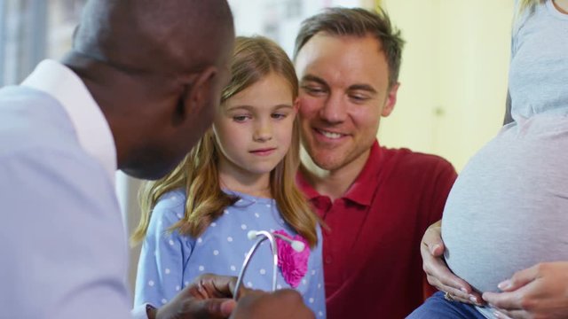  Doctor examining pregnant woman lets daughter listen to baby's heartbeat