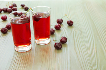 Two glasses of cherry juice and empty space.Left two glasses of cherry juice around scattered cherries, right empty space for text on light green background. Horizontal. Close. Daylight.