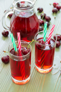2 cherry juices. Two glasses of cherry juice with straws in the foreground and in the background a jar full of cherry juice. Vertical. Daylight.