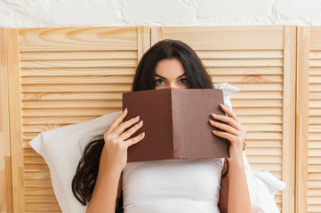 Beautiful young brunette woman hiding herself behind a book