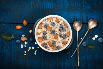 A healthy breakfast on a dark blue wooden background: Oatmeal, milk, blueberries, honey and almonds. Rustic style.