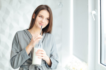Happy attractive young woman in grey bathrobe drinking milk