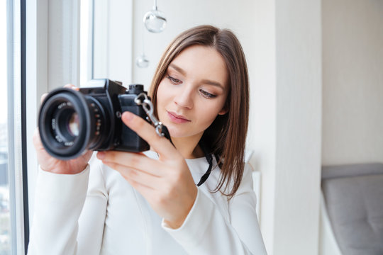 Concentrated woman using photo camera and taking pictures near window