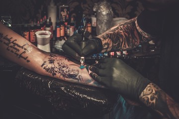 Professional tattoo artist makes a tattoo on a young girl's hand. - obrazy, fototapety, plakaty