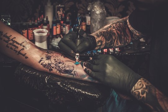 Naklejka Professional tattoo artist makes a tattoo on a young girl's hand.