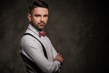 Stylish man with bow tie wearing suspenders and posing on dark background.