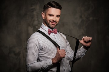 Stylish man with bow tie wearing suspenders and posing on dark background.