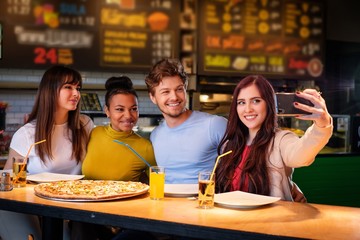 Cheerful multiracial friends taking selfie in pizzeria.