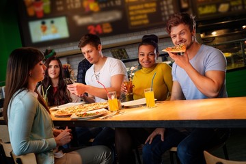 Cheerful multiracial friends having fun eating pizza in pizzeria.