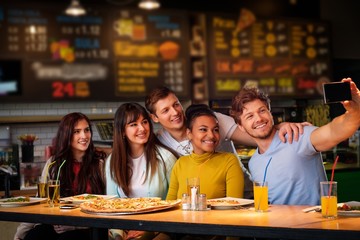 Cheerful multiracial friends taking selfie in pizzeria.