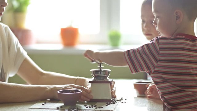 Twin brothers helping her mother to grind coffee in the kitchen in the morning.