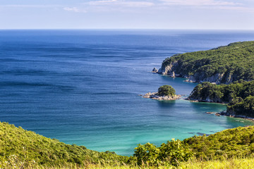 Island near shore of Russian resort area of the Sea of Japan with hills, clouds, rocks and greenery in sunny day