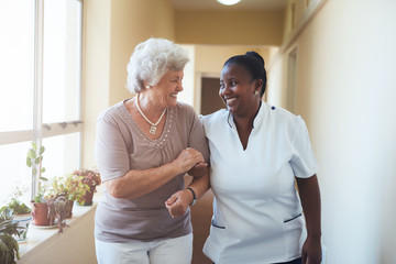 Glimlachende thuisverzorger en oudere vrouw die samen lopen