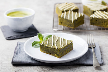 Matcha green tea brownie cake with white chocolate on a white plate Grey stone background
