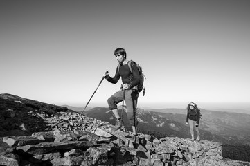 Young backpacker couple walking up rocky the mountain top, high altitude. Beautiful mountain landscape on the background. black and white