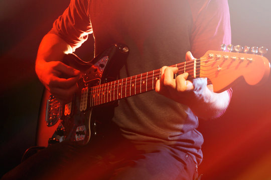 Young man playing on electric guitar on dark background with light effect