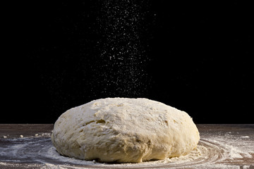 Fototapeta na wymiar dough is sprinkled with flour on black background