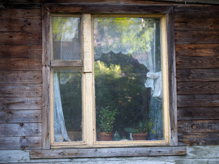 Window of country house. Wooden house, window, indoor plants, curtains, trees reflected in the glass. View oknnoy frame from the street