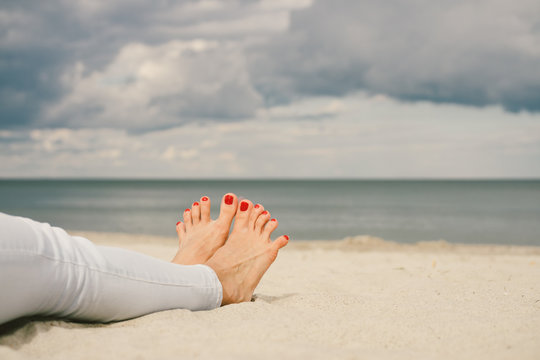 Barefoot female feet in jeans on the beach