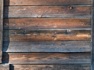 The wall of wooden village house. Old boards, sunlight. Texture of wooden boards.