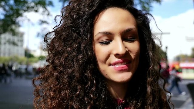 Portrait of happy young woman with beautiful curly hair sipping coffee in the city, slow motion