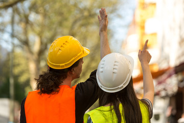 Back turned architects, a boy and a girl both with long hair, pointing at something at construction...