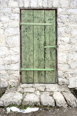 Fototapeta na wymiar Locked old green wooden door with part of exterior wall and snow on the ground