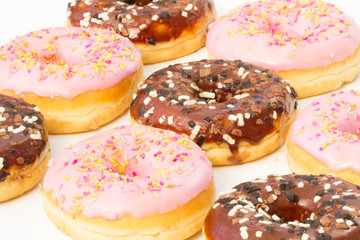 Rows of donuts with chocolate and pink icing and coloured sprinkles.