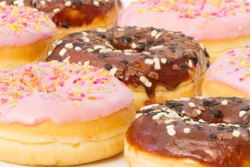 Rows of donuts with chocolate and pink icing and coloured sprinkles.
