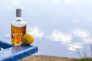 Bottle tequila and tumbler with lemon on shore of lake