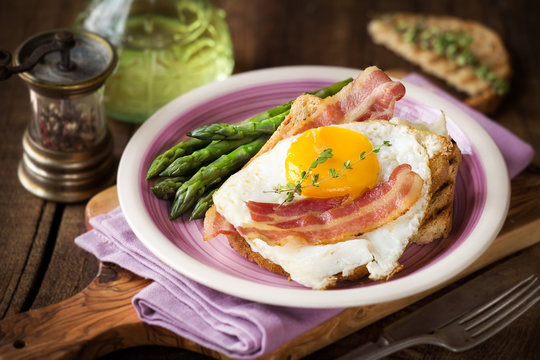 Delicious homemade breakfast with eggs, asparagus stalks, bacon and toast on dark rustic wooden background
